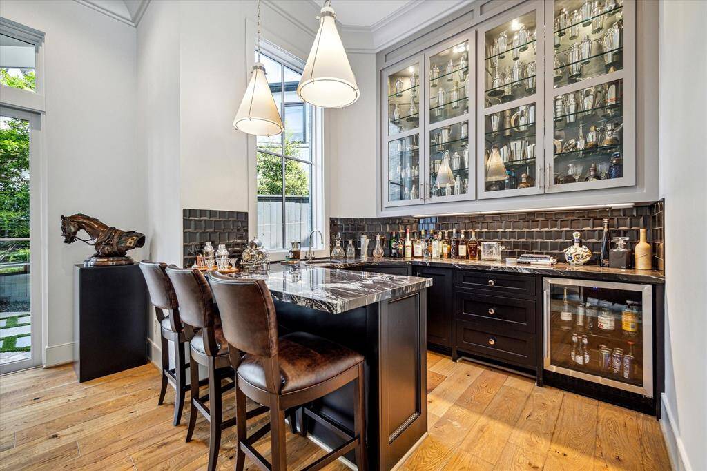 The elegant wet bar with dramatic marble countertops, has lighted glass-front cabinetry, under-counter beverage refrigerator, and ice maker