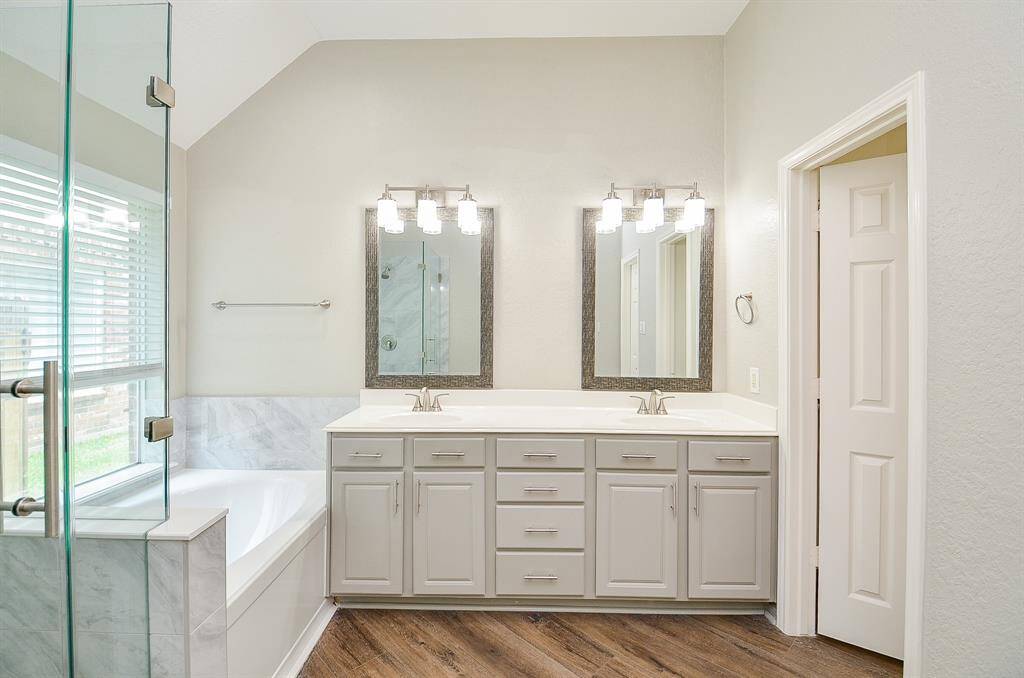 Pale walls and cabinetry lend a relaxed vibe to your primary ensuite bath; with trim dual sinks atop french white toned storage below, with gorgeous individual framed wall mirrors and delicate lighting, above. At left, are new soaking garden tub and new rimless walk-in, glass enclosed shower.