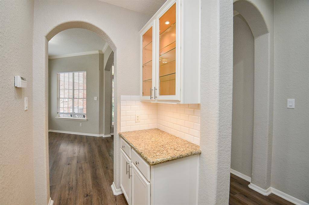 This divine butler's panty serves kitchen and living area entertainment needs, with warm granite counter top, pale tile backsplash and lit, glass front cabinetry, above.
