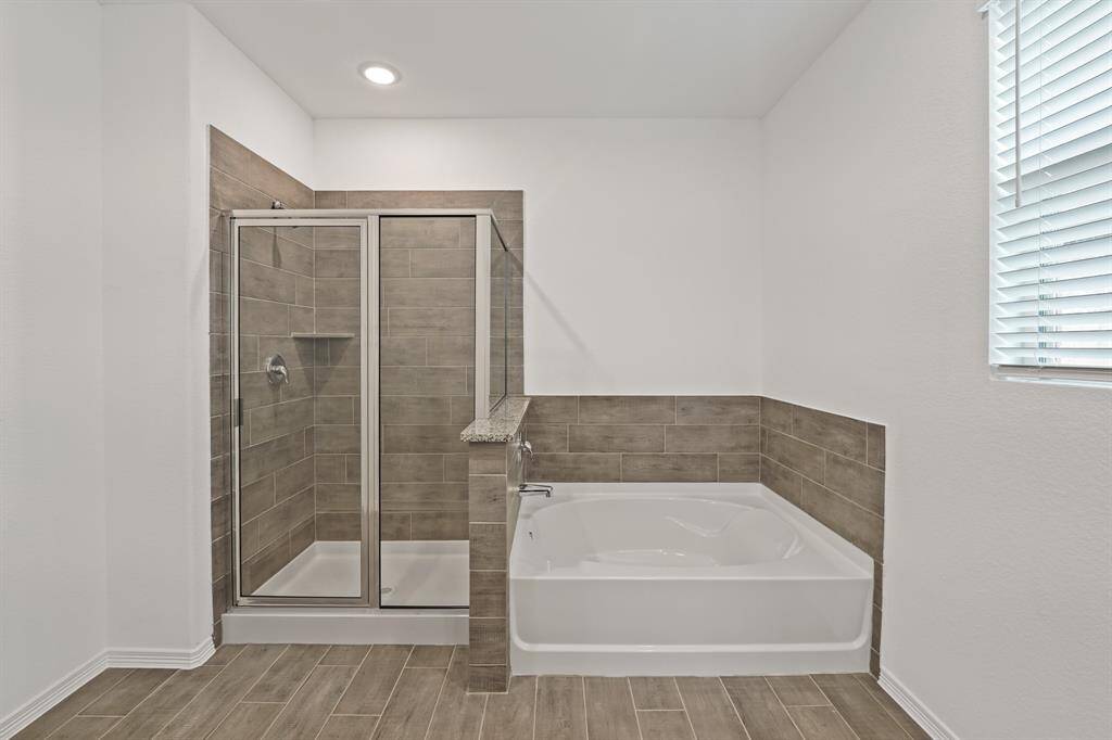 Spacious primary bath with a walk-in shower and separate soaking tub, both wrapped in neutral tile—creating a spa-like retreat.