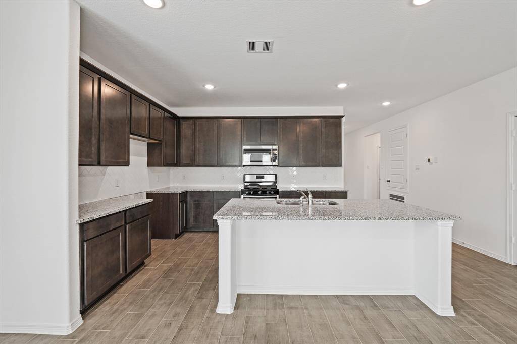 Modern kitchen with sleek dark cabinetry, granite countertops, stainless steel appliances, and a large center island—ideal for cooking and entertaining.