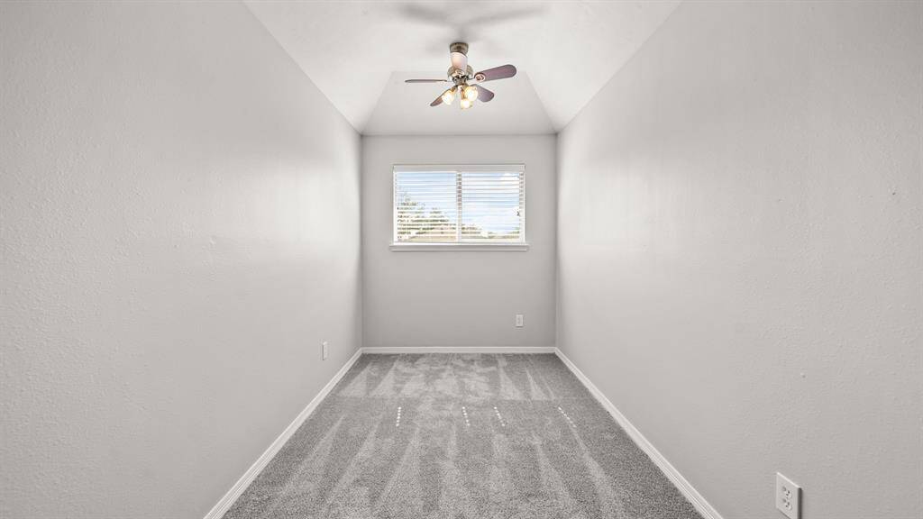 Additional space inside the loft, highlighted by carpet flooring, a ceiling fan, windows with privacy blinds, and a vaulted ceiling.