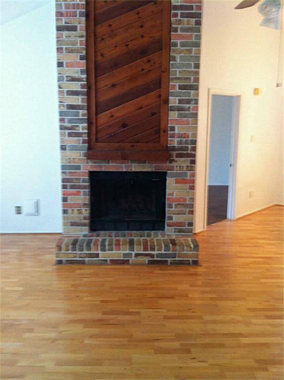 This photo features a cozy living area with a brick fireplace and wooden mantel. The room has hardwood flooring and neutral walls, providing a warm and inviting atmosphere.