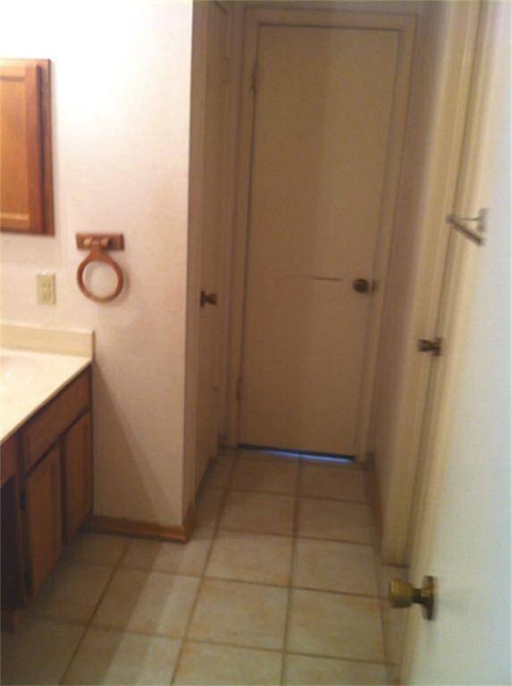 This is a compact bathroom with tiled flooring, a wooden vanity with a countertop, and a towel ring. The space includes a door, likely leading to a closet or another room.