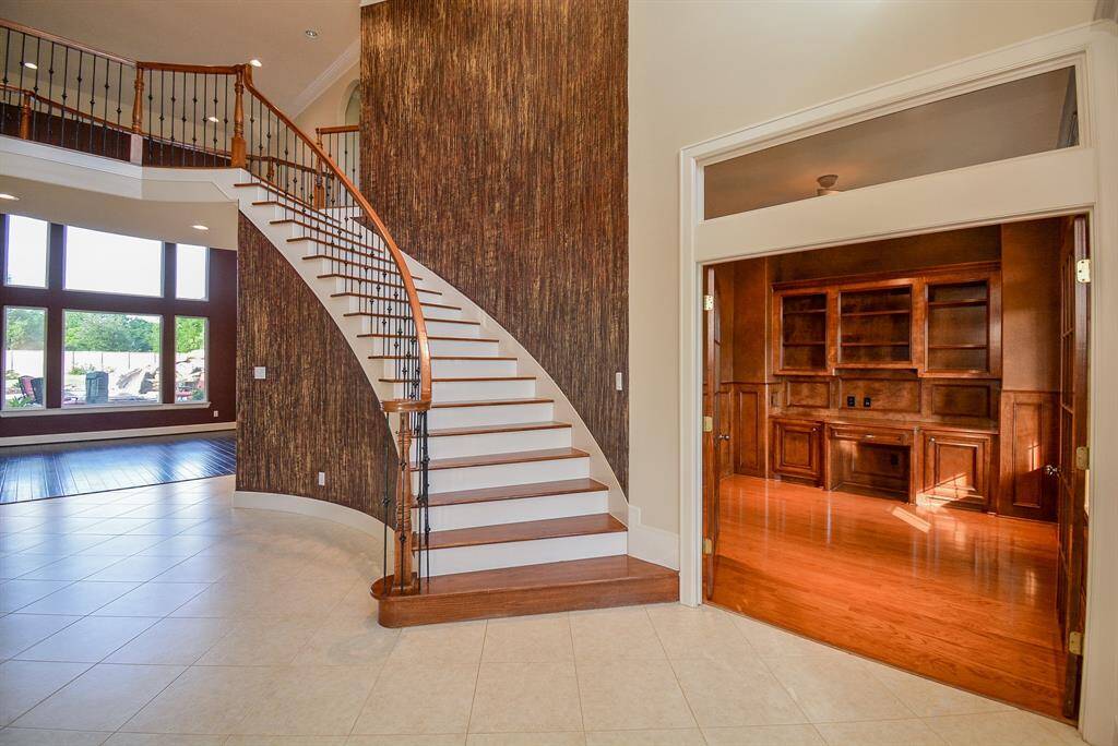 A clean, contemporary touch graces this sweeping staircase to the second level. Inside, natural features prevail in glistening wood appointments; seen here, right, in a wood-paneled study/den, with custom, wall-wide, built-in shelving, cabinetry and hardwood floor.