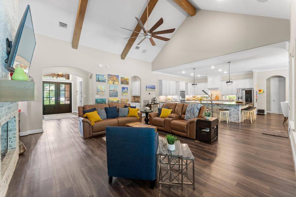 Luxury vinyl plank flooring creates a continuous, elegant feel throughout the main areas and primary suite. The heart of the home is a large, open living space featuring a family room with soaring vaulted ceilings and striking wood beams, seamlessly connecting to a gorgeous kitchen.