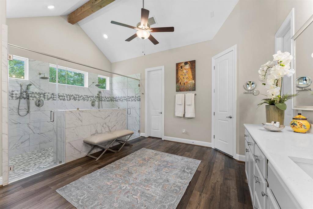 This luxurious large primary bathroom with cathedral ceiling and wood beams features two water closets, two vanities and two walk in closets with Elfa Shelving.