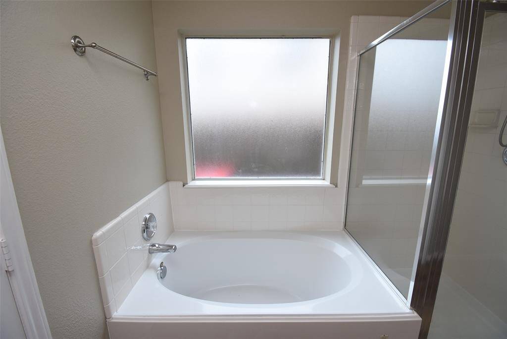 Relax and unwind in this inviting bathroom featuring a spacious soaking tub and a separate glass-enclosed shower. The frosted window provides natural light while maintaining privacy, creating the perfect spa-like retreat.