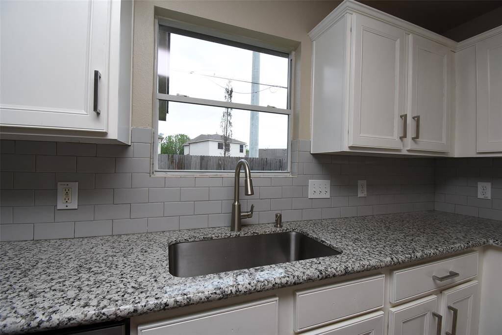 This beautifully upgraded kitchen features sleek white cabinets, a subway tile backsplash, and elegant granite countertops. The stainless-steel sink and high-arch faucet add a touch of sophistication to the space.