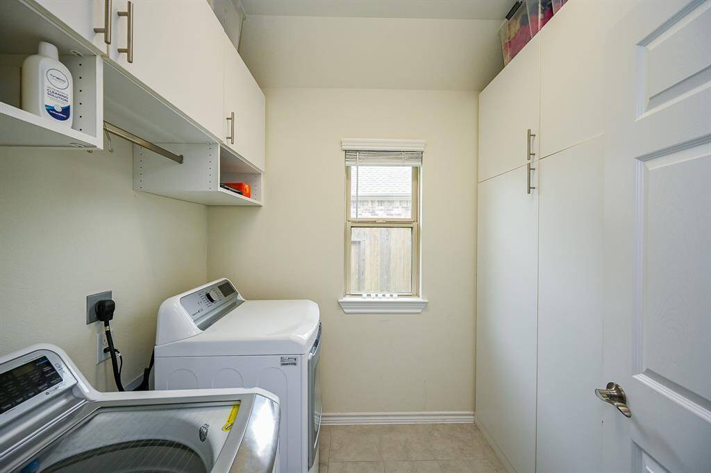 Well-organized laundry room with custom built in upper cabinets and side cabinets for storage, and a window for natural light.