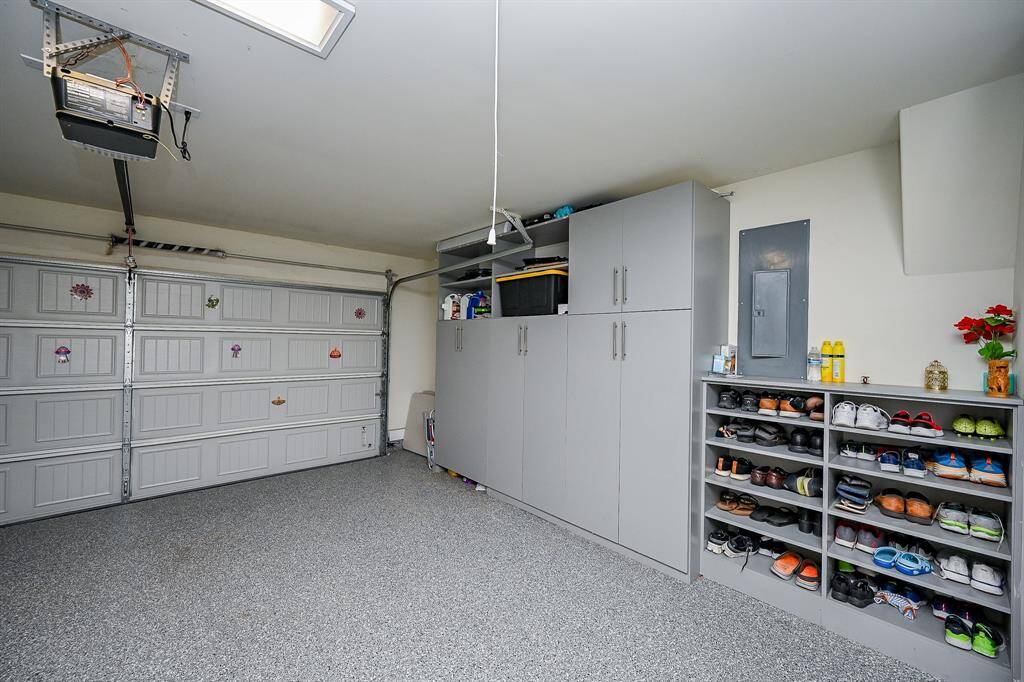 This garage features a clean, organized space with ample storage, including custom built in cabinets and a shoe rack. The floor is finished with a durable epoxy surface.
