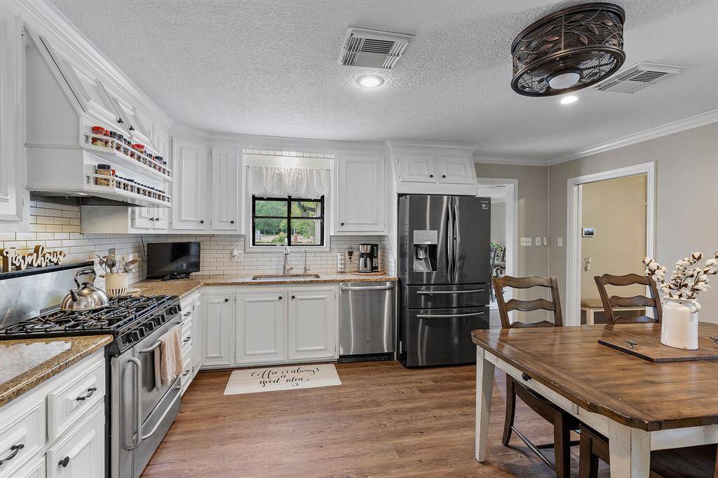 This kitchen is cozy and functional, featuring white cabinetry, stainless steel appliances, and a large black refrigerator. It includes a gas stove, ample counter space, and a nice dining area. The room is well-lit with a ceiling fan light and has a warm, inviting atmosphere.