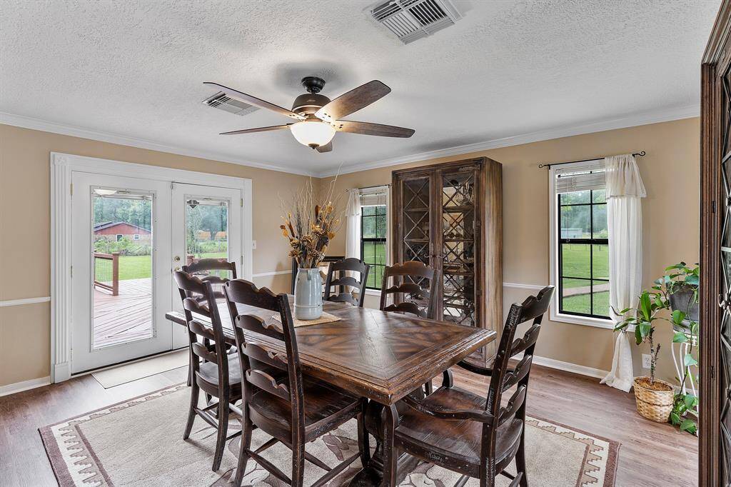 This dining room features a cozy, traditional design, a ceiling fan, and abundant natural light from large windows and French doors leading to a deck. The space is accented with neutral walls.