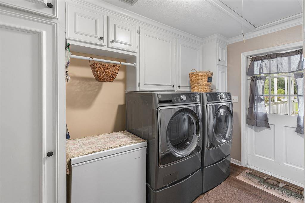 This laundry room features ample white cabinetry for storage. A door with a window allows natural light and leads to the outside deck, and hardwood flooring adds warmth to the space.