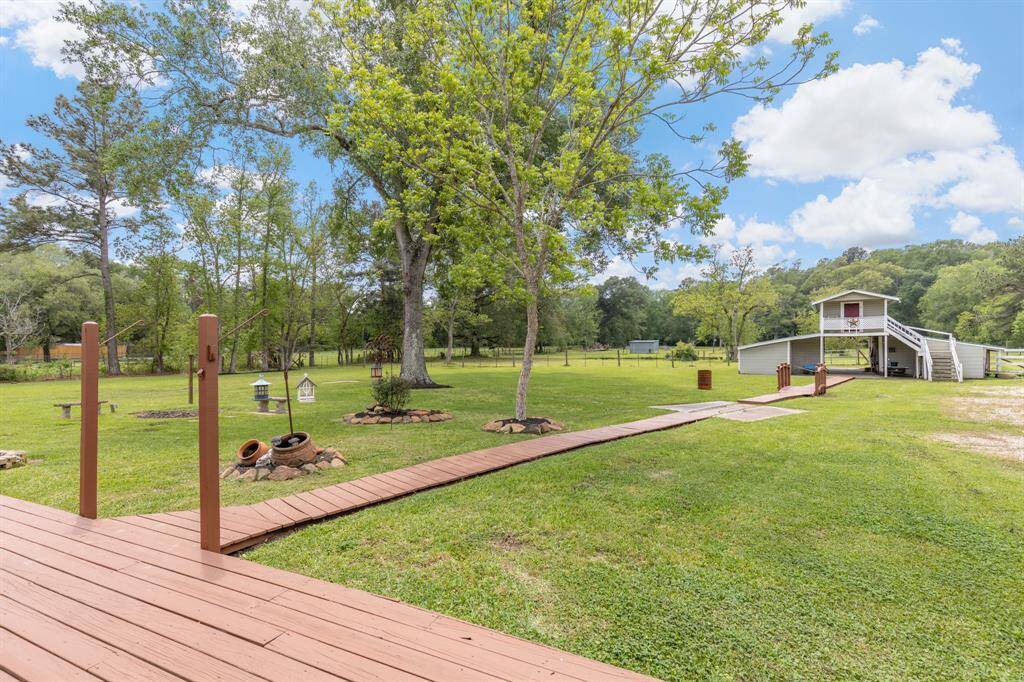 A spacious backyard with lush green grass and mature trees, featuring a wooden deck and pathway. Includes a barn with an apartment loft, also ideal for storage or hobby space, set against a serene, natural backdrop.