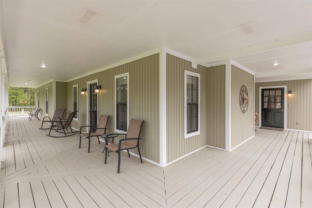 Spacious, covered wrap-around porch, perfect for relaxation. The porch features light decking and soft green siding, creating a welcoming and serene outdoor space.