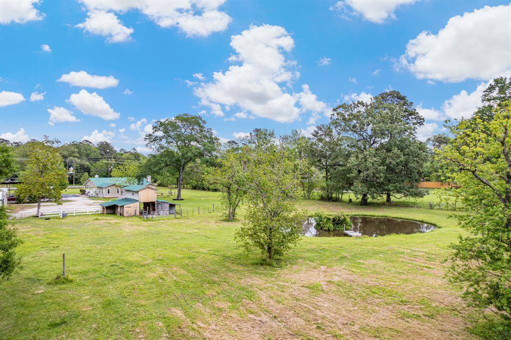 This serene property features a spacious grassy area, a small pond, and mature trees, creating a picturesque rural setting. A charming house and outbuildings are visible, ideal for a peaceful lifestyle.