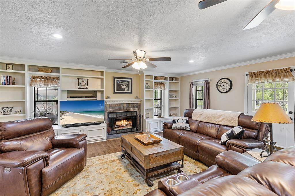 This cozy and spacious living room features a warm fireplace and built-in shelving. It is well-lit with natural light from multiple windows and has ceiling fans for comfort.