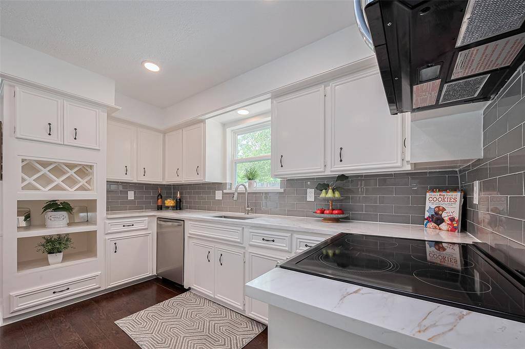 Beautifully updated kitchen featuring sleek quartz countertops, stainless steel appliances, and a stylish gray tile backsplash that perfectly complements the crisp white cabinetry."
