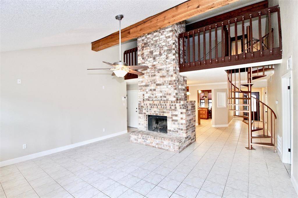 View of the living room with soaring ceilings and cozy fireplace. The spiral staircase leads to an upstairs game room.