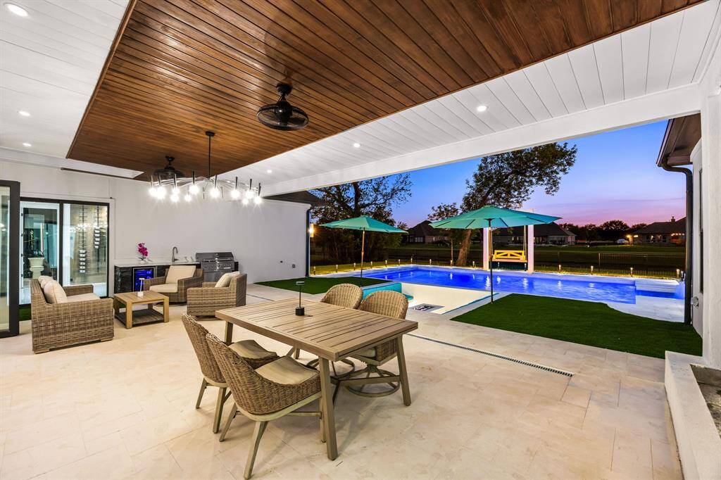 This beautifully designed outdoor living space seamlessly blends luxury and comfort, featuring a spacious covered patio with a stunning wood-paneled ceiling, integrated lighting, and a fully equipped outdoor kitchen perfect for al fresco dining. Enjoy resort-style relaxation beside a pristine, illuminated pool with a built-in spa and sleek water features. The thoughtfully landscaped yard and expansive views create an ideal backdrop for entertaining or unwinding at sunset.