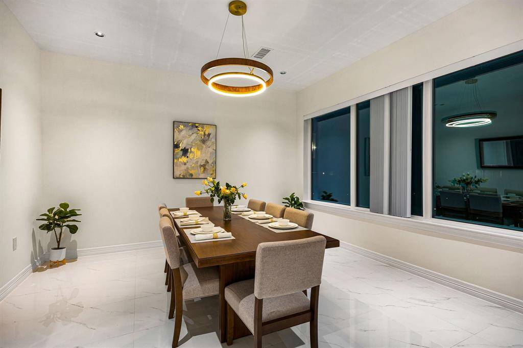Indulge in elegant dining experiences in this exquisite dining room, where sophistication meets modern design. A stunning contemporary chandelier casts a warm, ambient glow across the marble flooring, while soaring ceilings and a grand picture window with tailored blinds enhance the room’s airy elegance. The perfect setting for hosting unforgettable gatherings with family and friends.