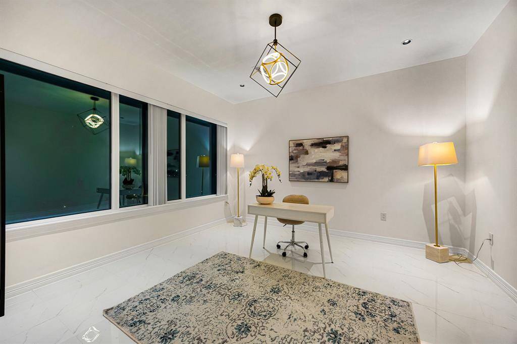 This sleek and sophisticated home office offers the perfect blend of style and functionality. Featuring glossy marble-look tile floors, contemporary lighting, and expansive windows that invite in natural light, the space is ideal for productivity in a serene, upscale setting.
