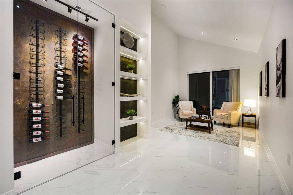 Step into this elegantly curated lounge featuring a stunning glass-enclosed wine display, custom lit shelving, and glossy marble-look tile floors. Perfect for entertaining or relaxing in style, this sophisticated space combines luxury with comfort, creating the ultimate setting for elevated living.