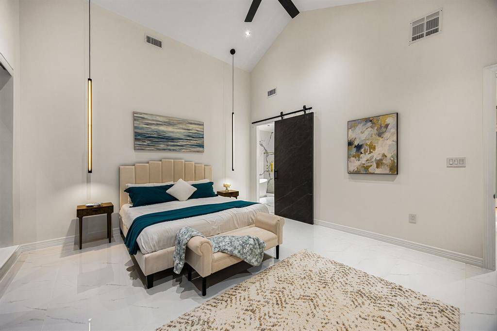 Experience elevated comfort in this stunning primary suite featuring soaring vaulted ceilings, sleek modern pendant lighting, and expansive sliding glass doors that open to a serene outdoor escape. Polished marble-look floors and a neutral palette create a refined, tranquil atmosphere—your private retreat awaits.
