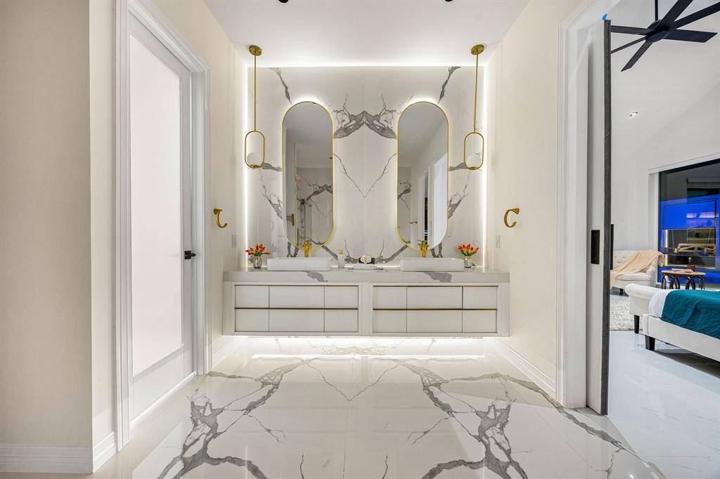 Step into spa-like sophistication in this luxurious en suite primary bathroom, featuring dramatic book-matched marble tile, designer pendant lighting, and floating vanity with integrated LED backlighting. Gold accents add a touch of opulence, while the seamless layout offers both style and serenity—your daily retreat redefined.