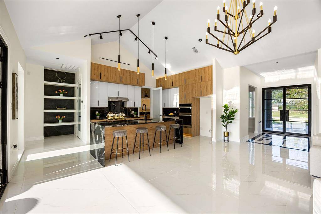 This breathtaking open-concept kitchen dazzles with soaring vaulted ceilings, striking modern lighting, and a seamless blend of natural wood and sleek finishes. Elegant black accents and high-gloss tile flooring complete the luxurious, contemporary design.
