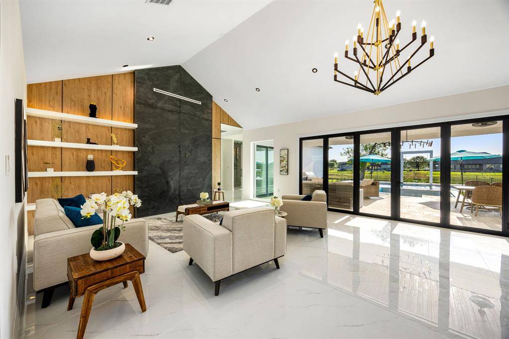 Bathed in natural light, this stunning living area features soaring ceilings, a dramatic feature wall, and expansive sliding glass doors that offer seamless indoor-outdoor living and breathtaking views of the backyard oasis.