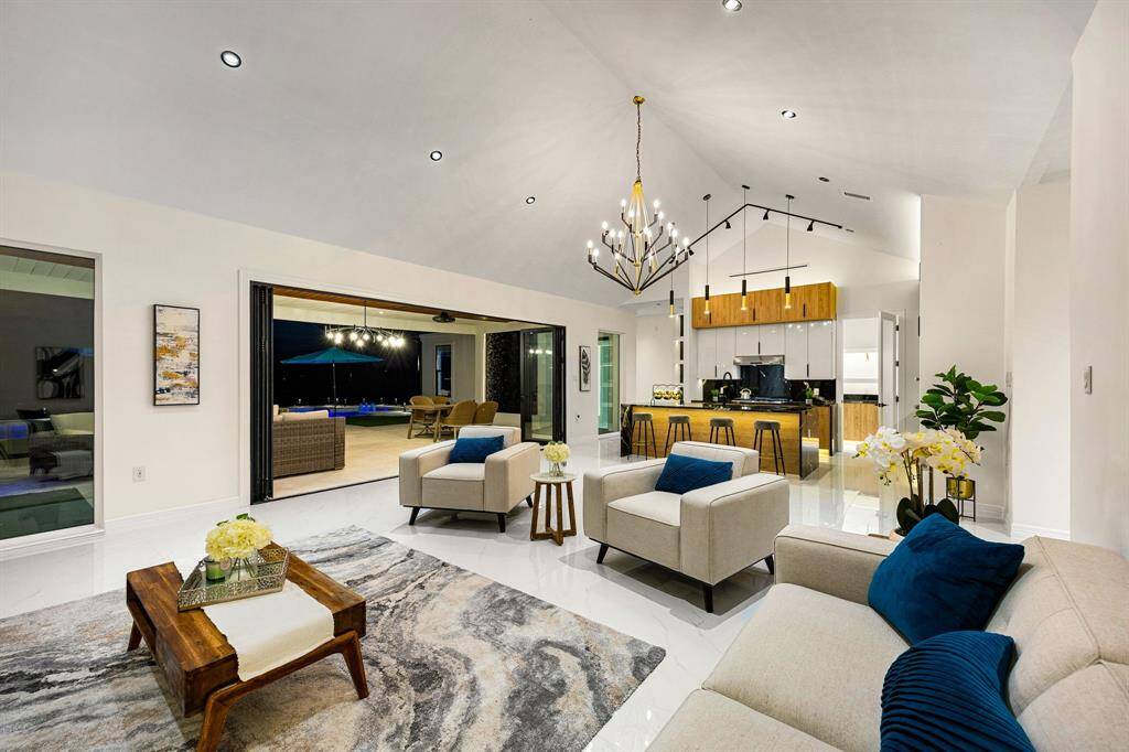 Step into this exquisite open-concept living space, where soaring vaulted ceilings and sleek recessed lighting create an airy, elegant ambiance. The seamless indoor-outdoor flow is highlighted by expansive glass sliders that lead to a covered patio and sparkling pool area. The gourmet kitchen boasts a striking combination of natural wood cabinetry, polished countertops, and modern pendant lighting, making it the perfect centerpiece for stylish entertaining and everyday living.