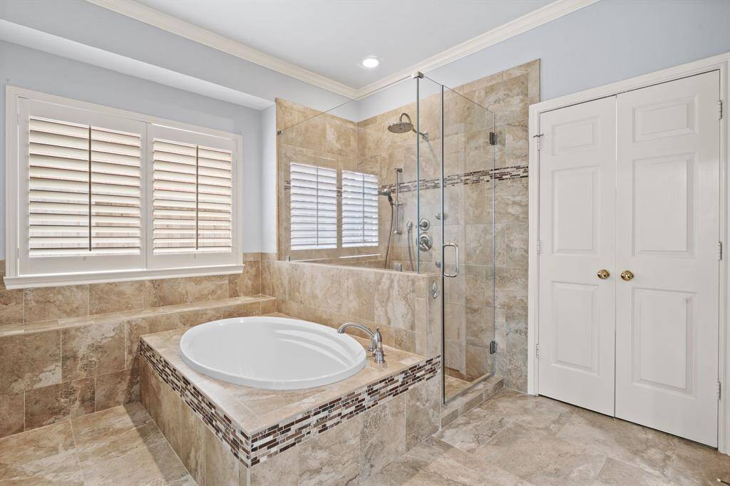 A large window fills the space with natural light, enhancing the serene atmosphere. The glass walk-in shower is outfitted with both a rain shower head and a handheld option, offering a spa-worthy experience.