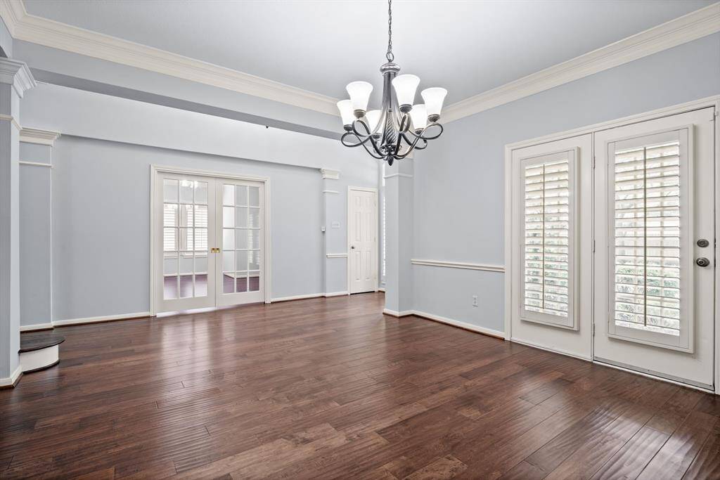 This stunning formal dining room showcases rich wood floors, classic crown and chair molding, a contemporary chandelier, and a private entrance to the front patio—perfect for sophisticated gatherings.