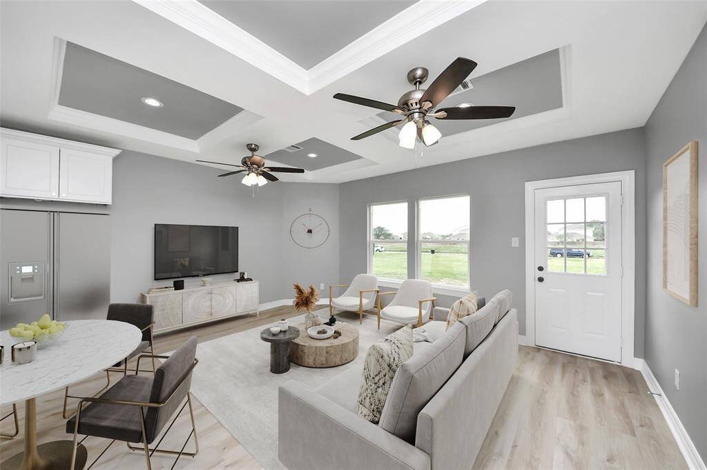 The family room is both bright and inviting, featuring durable LVP flooring, recessed lighting, and a stylish tray ceiling that adds architectural charm. Dual ceiling fans enhance airflow and comfort, while large windows allow natural light to pour in, creating a warm and welcoming atmosphere - virtually staged.