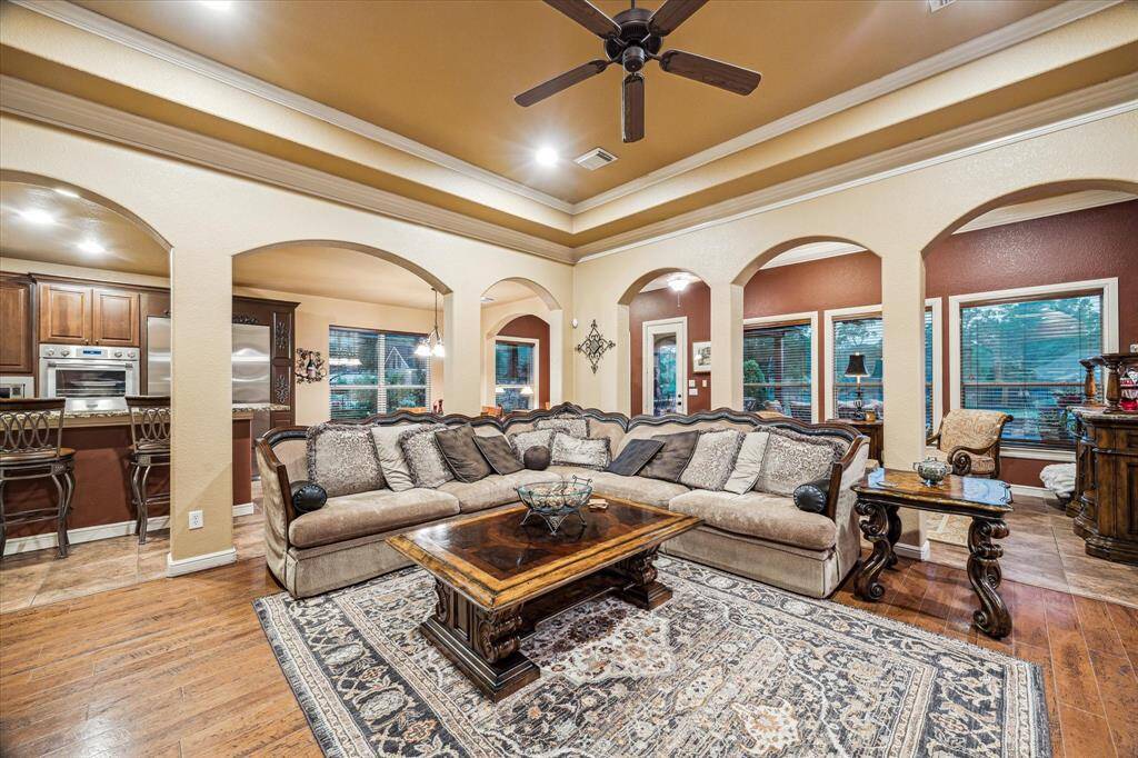 From this angle, the living room’s open-concept design flows seamlessly into the kitchen, breakfast area, and sunroom. Rich hardwood flooring transitions to tile for both style and functionality, while elegant arched openings and crown molding elevate the space. Large windows offer views of the backyard oasis, including the sparkling pool, summer kitchen, and outdoor living area with a cozy fireplace—perfect for year-round entertaining. This thoughtful layout blends indoor comfort with outdoor luxury.