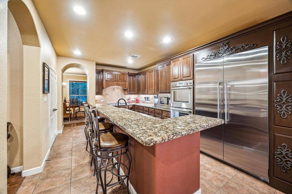 An alternate perspective shows off the kitchen’s full height cabinetry, professional-grade appliances, and expansive granite island—offering excellent flow into the living and dining areas.