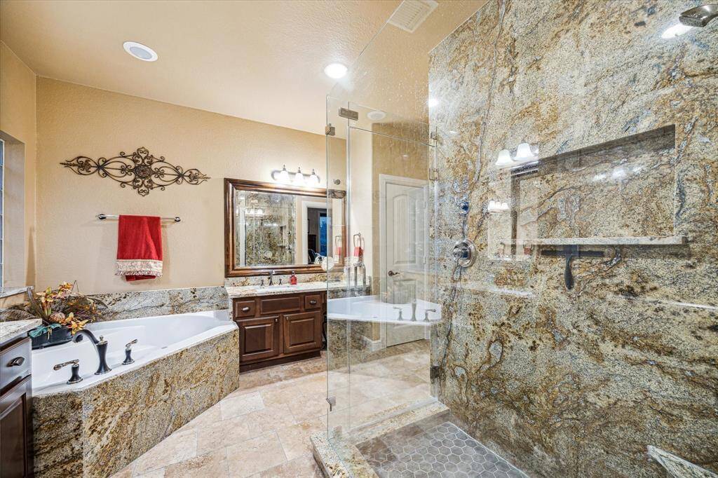 This primary bath features a stunning floor-to-ceiling granite shower with a built-in product niche, seamless Duraguard glass, and both a rain shower and wand with separate temperature and flow controls. Brizo nickel-plated and ebony fixtures add refined elegance throughout. The Jacuzzi tub is wrapped in rare granite, perfectly positioned beneath a glass block window for natural light and privacy.