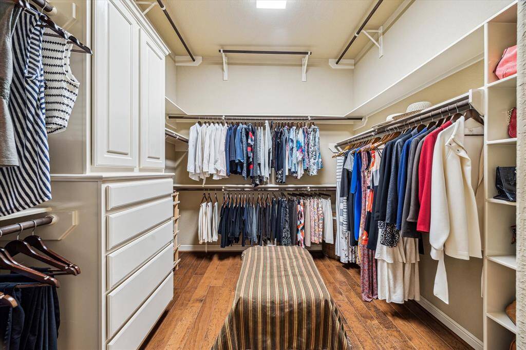 This generously sized walk-in closet features rich wood flooring and built-in storage, including custom shelving, drawers, and triple hanging rods for optimal organization. Thoughtfully designed with both function and style in mind, this closet offers ample space to keep everything neatly tucked away and easily accessible.