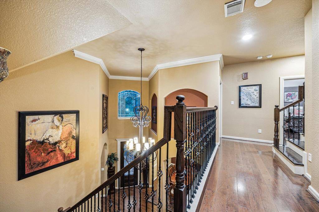 The upstairs landing offers an elegant transition between spaces, featuring hardwood flooring, crown molding, and wrought iron railings that overlook the entryway below. Thoughtfully lit with recessed and custom entry lighting, this open space provides access to upper-level bedrooms and bonus areas with both style and ease.