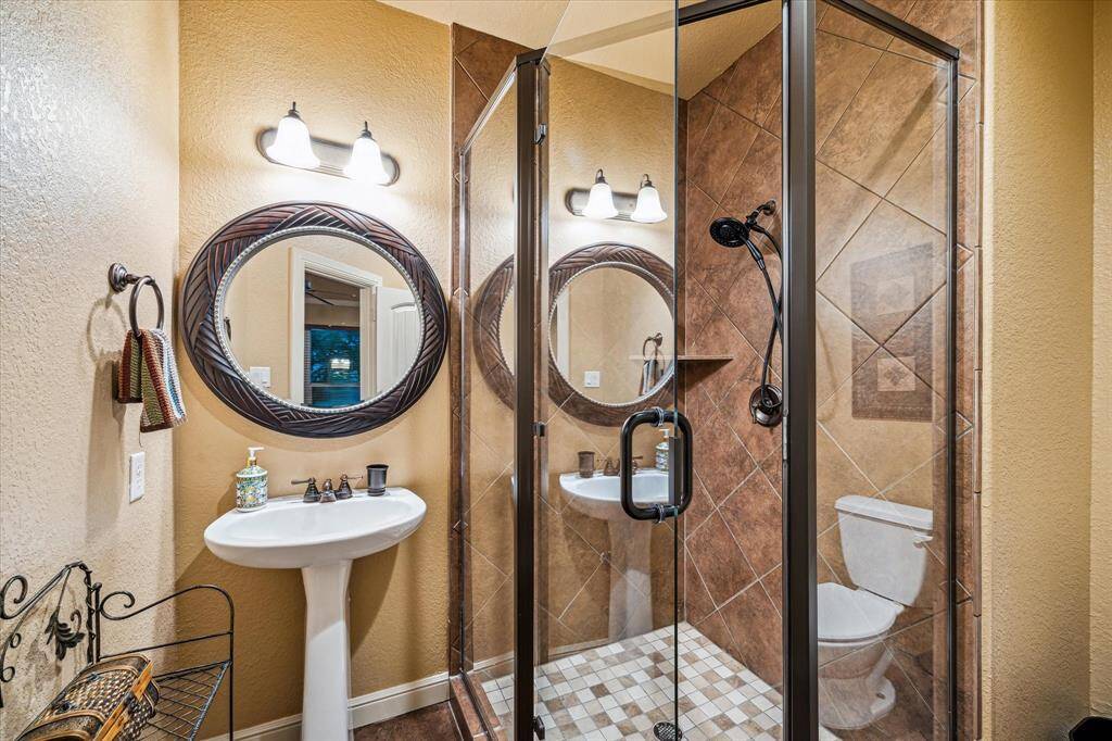 This stylish full bath, located just off the gym or optional fifth bedroom, features a sleek pedestal sink, oil-rubbed bronze fixtures, and a tiled walk-in shower with glass enclosure. Diagonal tile detailing adds a touch of sophistication, while the efficient layout makes it perfect for guest use or a private ensuite.