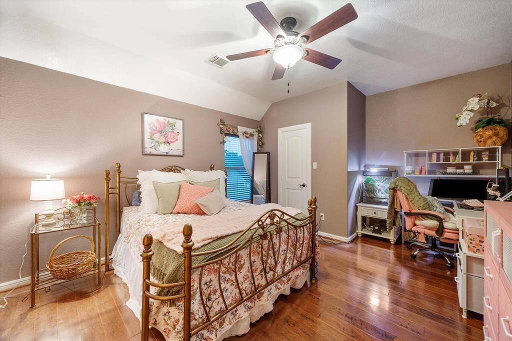 This inviting secondary bedroom features rich wood flooring, an angular ceiling with ceiling fan, and neutral tones that create a restful atmosphere. A walk-in closet offers ample storage, and the room’s generous size provides flexibility for added furnishings or a cozy reading nook.