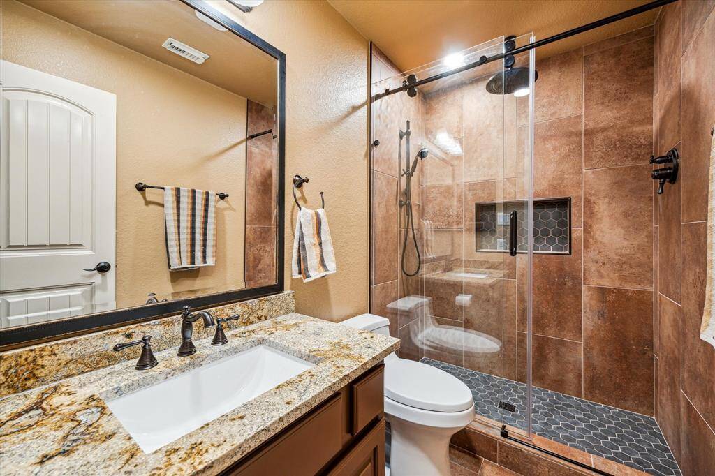 This beautifully updated full bath features a granite vanity with under-mount sink, bronze fixtures, and warm-toned cabinetry. The walk-in shower is finished with floor-to-ceiling tile, seamless glass enclosure, and a built-in niche for convenience and style. A perfect blend of function and elegance, ideal for guests.
