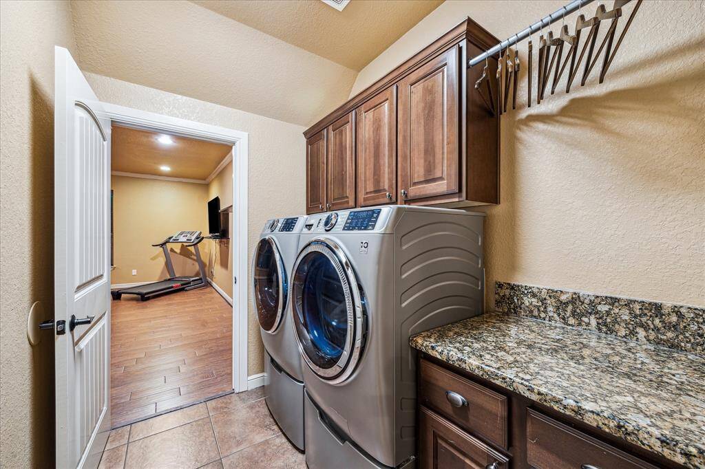Conveniently located, this well-equipped utility room features granite countertops, upper and lower cabinetry for ample storage, and a hanging rod for easy laundry organization. Tile flooring offers durability, and the space also houses the home’s freezer—ideal for additional food storage. With direct access to the adjacent fifth bedroom or gym, this space is as functional as it is efficient.