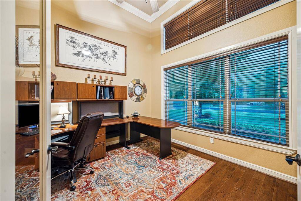 The versital home office showcases rich wood flooring, high ceilings, and a wide window with blinds that fills the space with natural light. An ideal spot for a private study, library, or work-from-home setup.