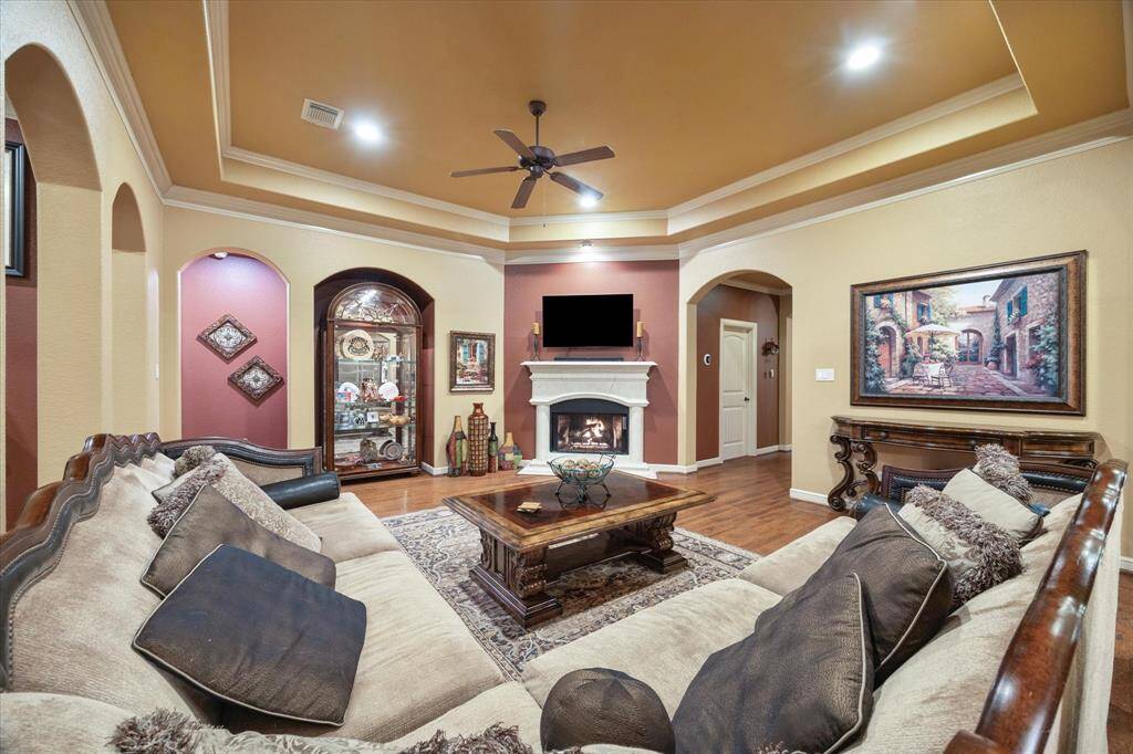 This cozy living room also showcases warm tones, a beautiful tray ceiling, and rich hardwood floors. Elegant archways and a striking stone fireplace create an inviting focal point, while a built-in alcove adds architectural interest. Perfect for both relaxing and entertaining.