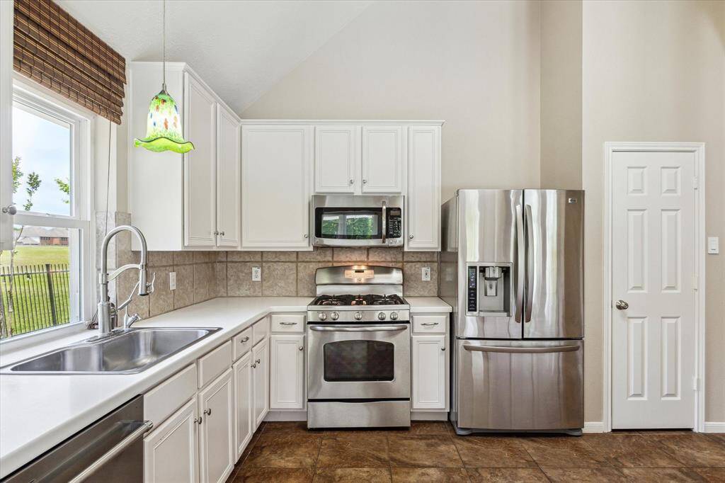 Kitchen features Corian countertops, refaced cabinets, stainless steel appliances which include microwave, oven with gas range and refrigerator. Pantry door on the right provides plenty of food storage space.