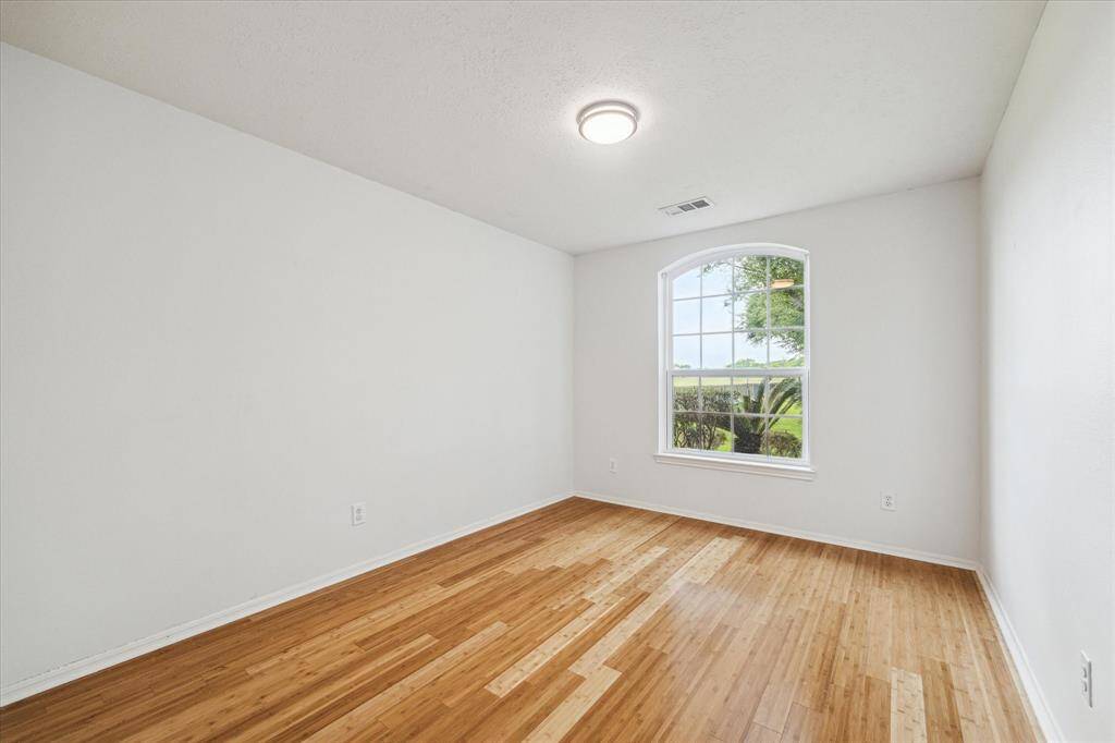 The secondary bedroom features bamboo wood flooring, fresh paint, a simple light fixture, and a window that brings in natural light.