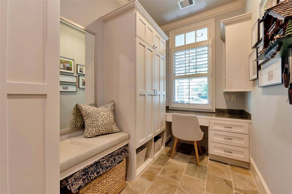 This charming mud room features built-in cabinetry, a cozy bench with storage, and a dedicated desk space under a bright window. Slate flooring adds warmth and texture, making it the perfect blend of function and comfort for work or organization.